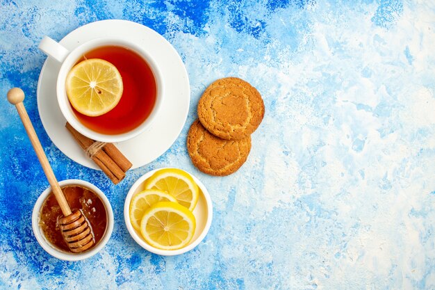 파란색 테이블 여유 공간에 있는 볼 비스킷 레몬 조각에 있는 차 꿀의 상위 뷰 컵