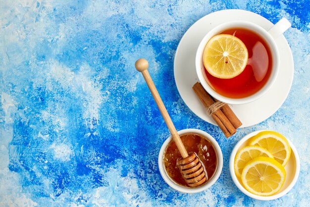 Top view cup of tea honey in bowl lemon slices on blue table free space