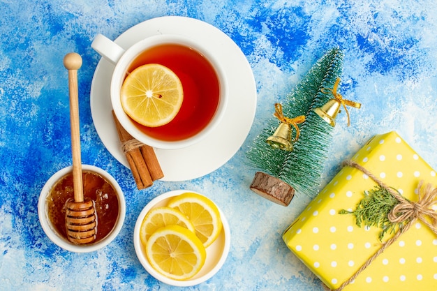 Free photo top view cup of tea honey in bowl lemon slices small xmas tree yellow gift on blue table