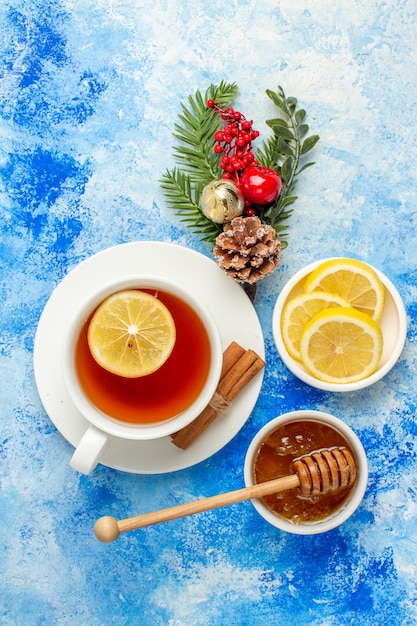 Top view cup of tea honey in bowl lemon slices xmas tree branches on blue table