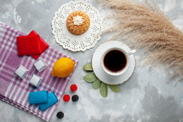 Vista dall'alto della tazza di tè caldo all'interno della tazza bianca con cioccolatini al limone sulla luce, torta di caramelle al cioccolato del tè