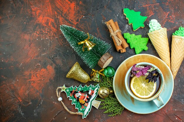 濃い赤のテーブルにお茶のアイスクリームシナモンスティッククリスマスツリークッキークリスマスオーナメントのトップビューカップ