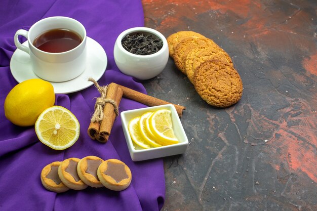 Top view cup of tea lemon slices in bowl cinnamon sticks tea in bowl on purple tablecloth notepad on dark red table