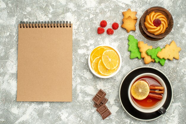 Top view cup of tea lemon slices in bowl notebook on grey surface