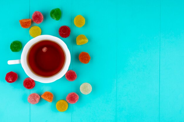 Top view of cup of tea and marmelads on blue background with copy space