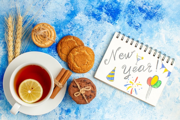 Foto gratuita vista dall'alto tazza di tè capodanno scritto sui biscotti del taccuino sul tavolo blu