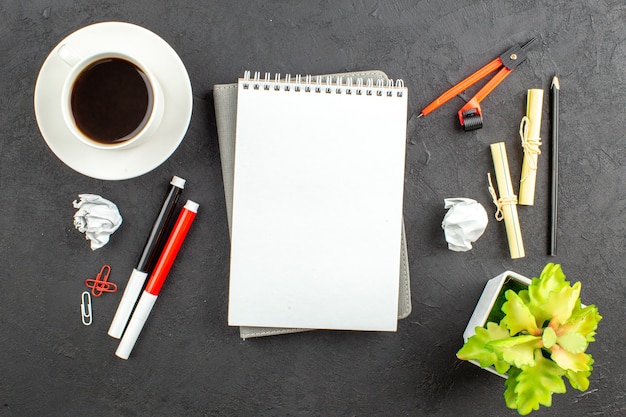 Top view cup of tea red and black markers binder clips compasses notebook on black table