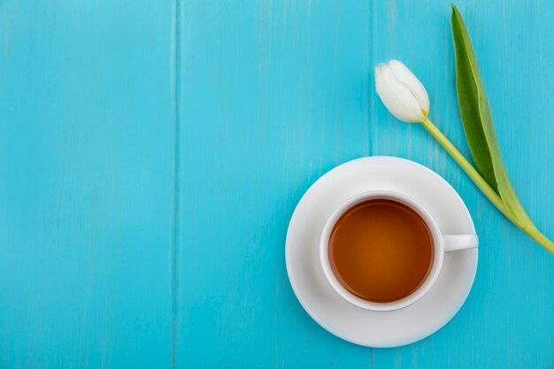 Вид сверху чашки чая на блюдце и цветок на синем фоне с копией пространства