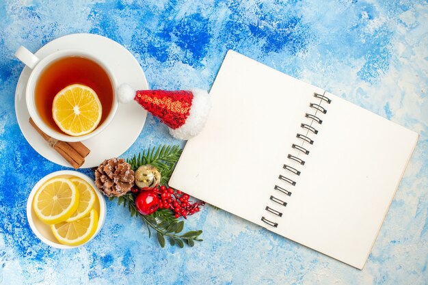 Top view a cup of tea small xmas tree branch lemon slices notepad on blue table