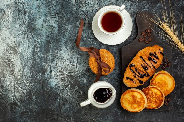 Top view of a cup of tea and tasty breakfast with pancakes croisasant on dark table