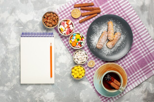 Top view of cup of tea with bagels marshmallow and candies on white surface