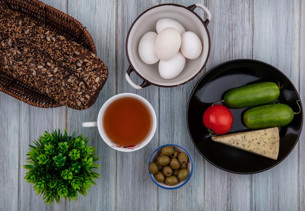 접시에 검은 빵 치즈 오이, 토마토와 회색 배경에 냄비에 닭고기 달걀과 올리브 차의 상위 뷰 컵