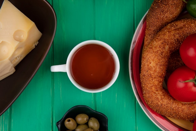 Вид сверху на чашку чая с булочками на тарелке с оливками на миске на зеленом деревянном фоне