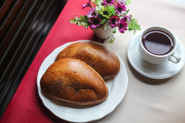 Top view cup of tea with buns on the table and with flowers