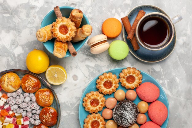 Top view cup of tea with cakes cookies and macarons on white surface