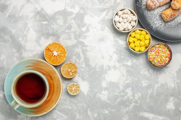 Top view of cup of tea with candies and bagels on white surface