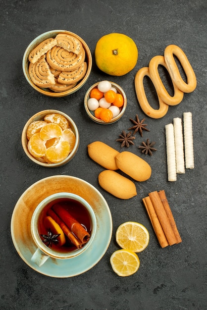 Top view cup of tea with candies biscuits and fruits on grey table tea sweet cookie