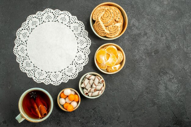 Top view cup of tea with candies and biscuits on grey table tea sweet cookies