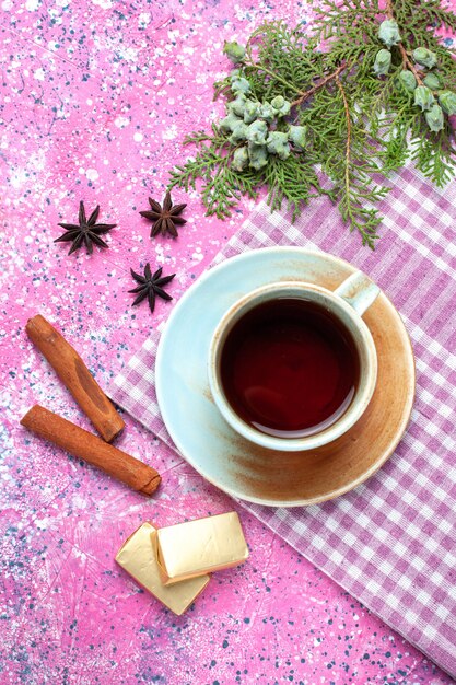 Top view cup of tea with candies and cinnamon on pink desk.