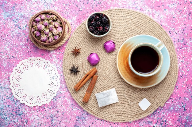 Top view cup of tea with candies and cinnamon on pink desk.