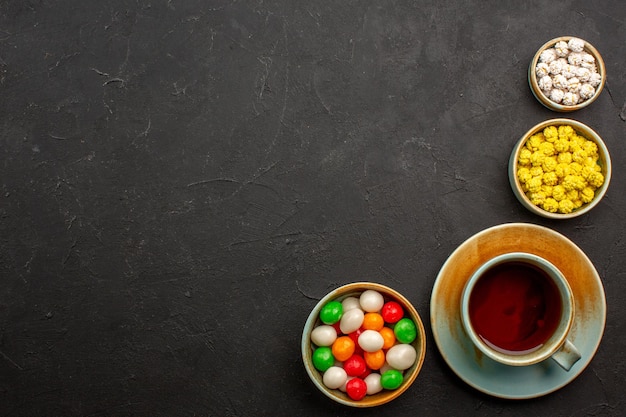 Top view cup of tea with candies on dark desk tea color rainbow candy