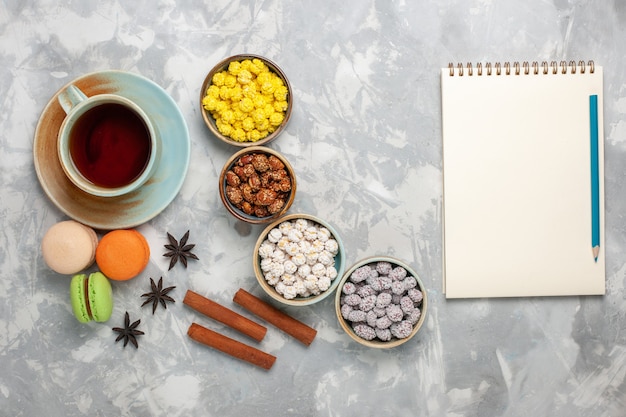 Top view cup of tea with candies and french macarons on light-white desk