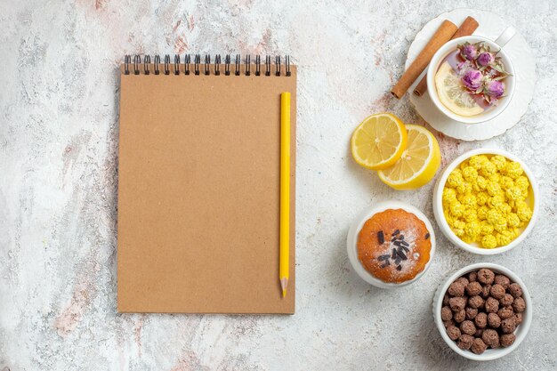 Top view cup of tea with candies and lemon slices on light-white space