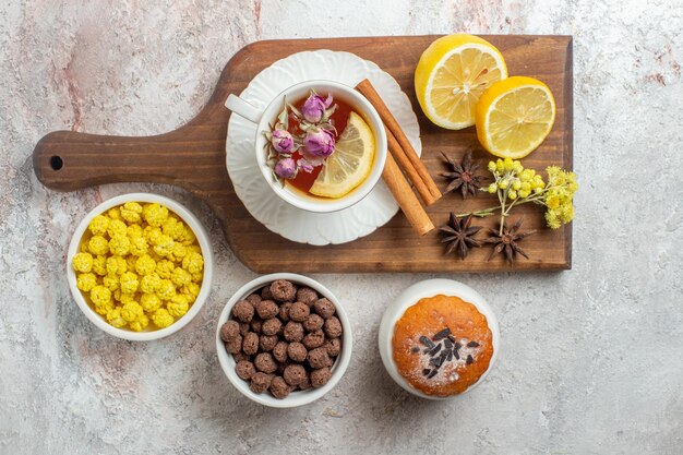 Top view cup of tea with candies and lemon slices on a white space