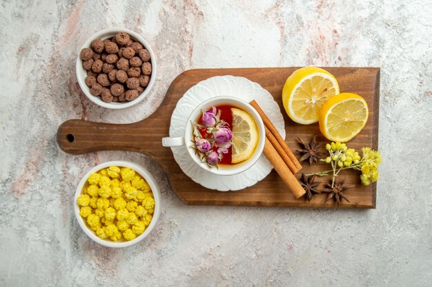 Top view cup of tea with candies and lemon slices on white space