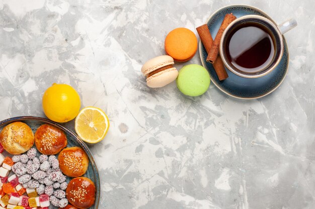 Top view cup of tea with candies and little cakes macarons on white surface