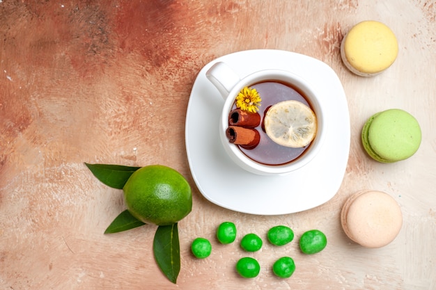 Top view cup of tea with candies and macarons on light brown table tea lemon biscuit