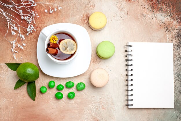 Top view cup of tea with candies and macarons on a light table tea lemon biscuit