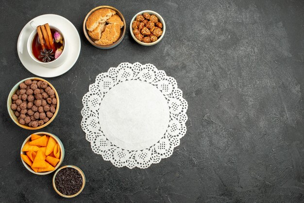 Top view cup of tea with candies and nuts on dark-grey surface tea drink candy