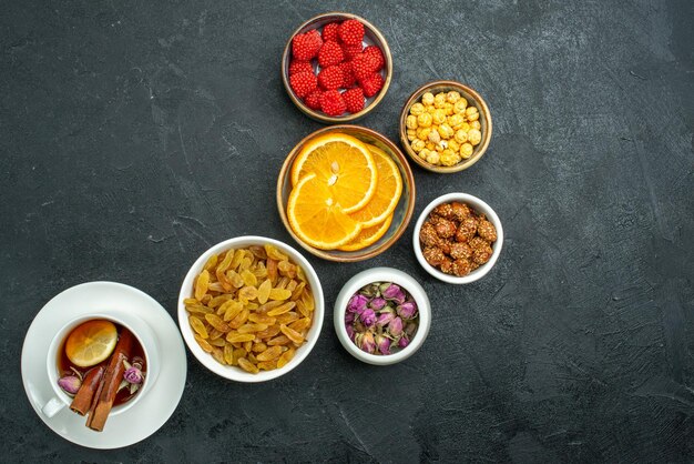 Top view cup of tea with candies nuts and orange slices on dark surface confiture tea candy sweet