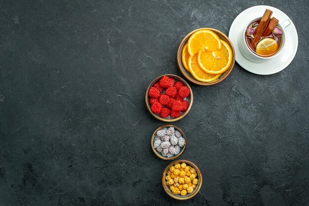 Top view cup of tea with candies and orange slices on a dark surface confiture tea candy sweet