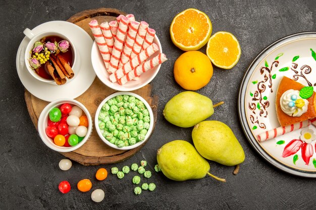 Top view cup of tea with candies pears and tangerines on dark space