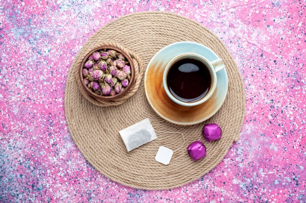 Top view cup of tea with candies on pink background.