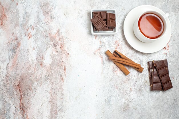 Top view of cup of tea with chocolate bars on white surface