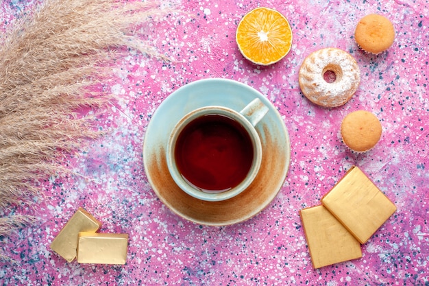 Vista dall'alto della tazza di tè con caramelle al cioccolato e torte sulla superficie rosa