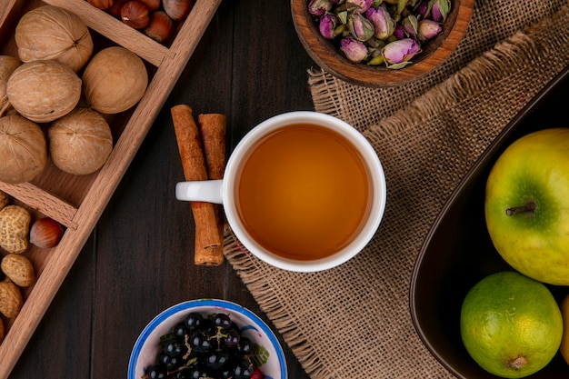 Вид сверху чашки чая с корицей, яблоками и орехами на деревянной поверхности