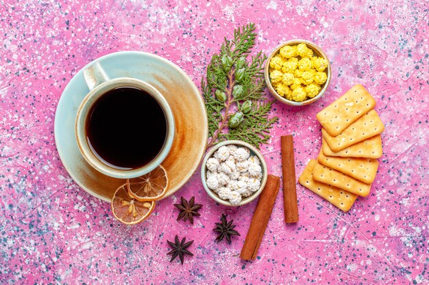 Вид сверху чашка чая с коричными конфетами и крекерами на розовом столе, конфетный чай, напиток хрустящего цвета