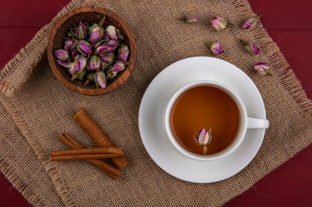 Top view a cup of tea with cinnamon and dry rosebuds on a beige napkin