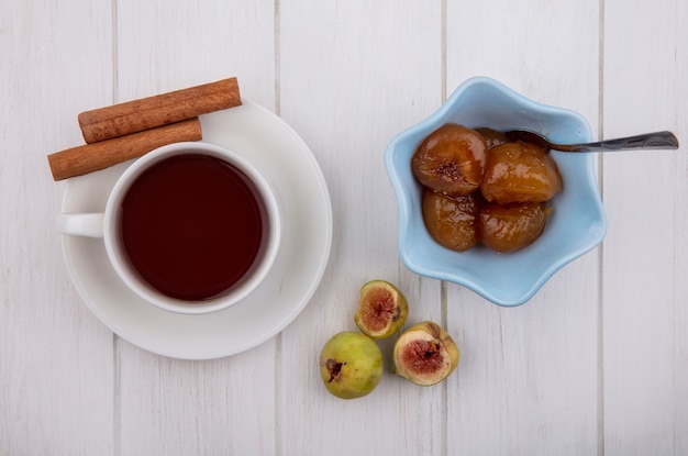 Top view cup of tea with cinnamon  fig jam in saucer with teaspoon on white background