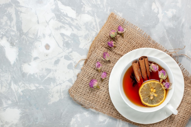 Top view cup of tea with cinnamon and lemon on white surface