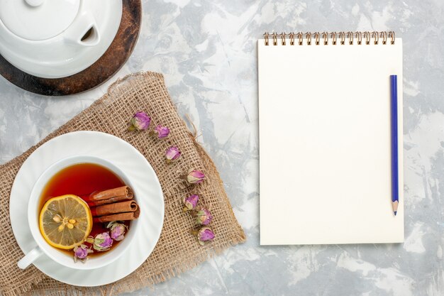 Top view cup of tea with cinnamon notepad and lemon on white surface