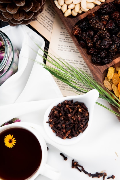 Foto gratuita vista dall'alto di una tazza di tè con chiodi di garofano spezie in una ciotola e noci miste e frutta secca in una scatola di legno alle pagine del libro