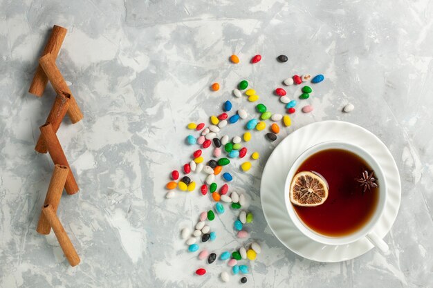 Top view cup of tea with colorful different candies and cinnamon on light-white desk