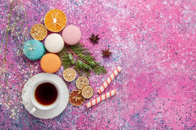 Top view cup of tea with colorful french macarons on the pink surface