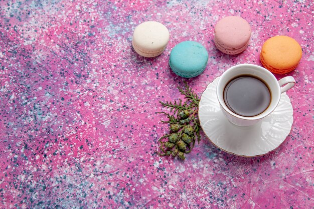 Вид сверху чашка чая с красочными французскими макаронами на розовой стене, торт, бисквит, сладкий пирог