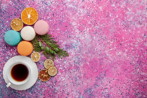 Top view cup of tea with colorful french macarons and waffles on pink floor cake biscuit sugar sweet pie tea